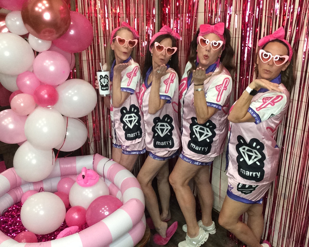 Girls night in matching outfits with 'Marry' on them, surrounded by pink and white balloons.